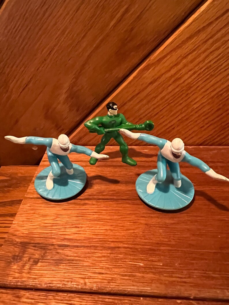 May include: Three plastic action figures, two in blue and white and one in green. The blue figures are on blue and white bases. The green figure is holding a green staff.
