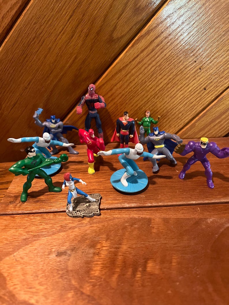May include: A collection of superhero action figures, including Superman, Batman, Spiderman, The Flash, and others. The figures are made of plastic and are painted in various colors.