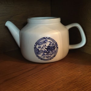 May include: White teapot with a blue and white floral design. The design features a pagoda and a bridge.