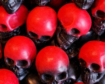 Op de afbeelding: Een close-up van een stapel rood en zwart schedelvormige objecten. De schedels zijn felrood aan de bovenkant, overgaand in zwart bij de kaaklijn. De objecten zijn bij elkaar gegroepeerd, wat een griezelige Halloween-themaweergave creëert.