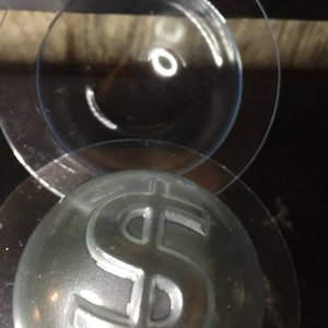 May include: A clear glass dome with a dollar sign embossed on the top. The dome is sitting on a black surface.