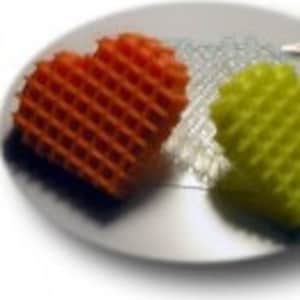 May include: Two heart-shaped waffle cookies, one orange and one yellow, on a white plate.