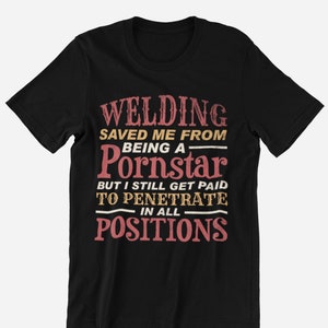 May include: Black t-shirt with a distressed text design in red, beige, and white. The text reads "WELDING SAVED ME FROM BEING A Pornstar BUT I STILL GET PAID TO PENETRATE IN ALL POSITIONS."