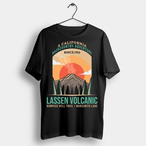 May include: Black t-shirt featuring a graphic of a mountain with a rising sun, trees, and the text "A California Backcountry Adventure Since 1916." Below, it reads "Lassen Volcanic, Bumpass Hell Trail - Manzanita Lake."
