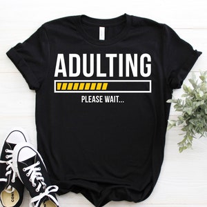 May include: Black t-shirt with white text that reads "Adulting" with a yellow progress bar underneath and the text "Please wait..." below the progress bar.