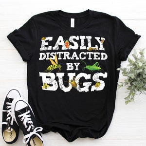 May include: Black t-shirt with white text that reads "Easily Distracted by Bugs". The text is surrounded by images of various bugs, including a grasshopper, a beetle, and a wasp.