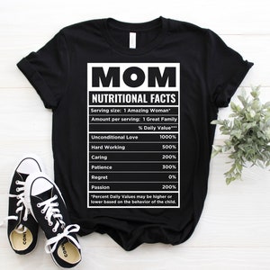 May include: Black t-shirt with a white graphic that reads "MOM NUTRITIONAL FACTS." The graphic lists values for Unconditional Love, Hard Working, Caring, Patience, Regret, and Passion. Black and white sneakers are in the foreground.
