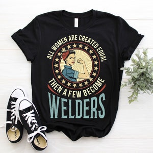 May include: Black t-shirt featuring a vintage-style graphic of a woman with her fist raised. The graphic reads "All women are created equal then a few become welders".