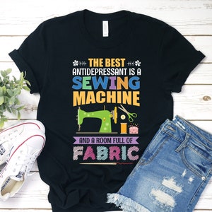 May include: Black t-shirt with the text "THE BEST ANTIDEPRESSANT IS A SEWING MACHINE AND A ROOM FULL OF FABRIC." The design includes a green sewing machine, scissors, and spools of thread. White trainers and denim shorts are also in the image.