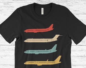May include: Black t-shirt featuring four colorful airplane illustrations in red, beige, teal, and yellow. The vintage-style graphic design showcases the side profiles of the aircraft, perfect for aviation enthusiasts.