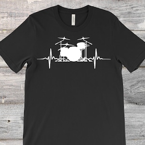 以下が含まれることがあります： 黒いTシャツ。白いグラフィックは、心拍ラインに統合されたドラムセットです。デザインにはドラム、シンバル、スタンドが含まれており、音楽的なテーマを作成します。シャツは柔らかい素材で作られています。