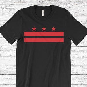 May include: Black t-shirt with a red and white design of the District of Columbia flag. The flag features three red stars and two red horizontal stripes.