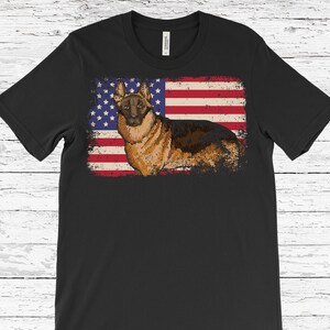 May include: Black t-shirt with a distressed American flag design and a German Shepherd dog illustration. The flag features red and white stripes and a blue star field. The dog is brown and black.
