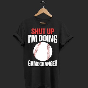 Könnte beinhalten: Schwarzes T-Shirt mit weißem Text, der "Shut Up I'm Doing Gamechanger" lautet, und einem weißen Baseball mit roten Nähten.