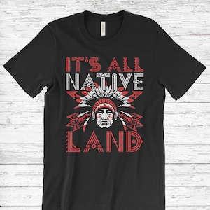 May include: Black t-shirt with a red and white graphic design. The graphic features a Native American headdress and the text "It's All Native Land".