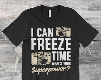 May include: Black t-shirt with the text "I CAN FREEZE TIME WHAT'S YOUR Superpower?" and two vintage camera illustrations in beige. A casual tee for photographers and photography enthusiasts.
