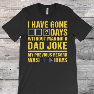 May include: Black t-shirt with yellow text that reads "I HAVE GONE 0 DAYS WITHOUT MAKING A DAD JOKE" and "MY PREVIOUS RECORD WAS 0 DAYS". The text is in a bold, sans-serif font.