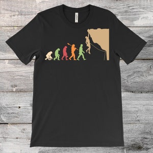 May include: A black t-shirt featuring a graphic of human evolution culminating in a person rock climbing. The graphic is in a vintage style with different colours for each stage of evolution.