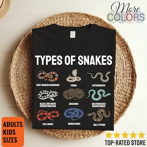 May include: A black t-shirt featuring the white text TYPES OF SNAKES above nine illustrations of snakes, including a grey-banded kingsnake, cobra, cottonmouth, black and white Kenyan sand boa, anaconda, San Francisco garter snake, milk snake, indigo snake, and ball python.