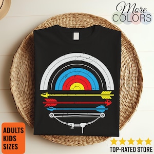 Op de afbeelding: Zwart t-shirt met een distressed boogschietdoelontwerp in wit, blauw, rood en geel. Onder het doel bevinden zich drie pijlen. Het shirt heeft ook de tekst "More Colors", "Adults Kids Sizes" en "Top-Rated Store".