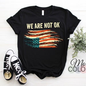May include: Black t-shirt with a distressed American flag design and the text "WE ARE NOT OK".