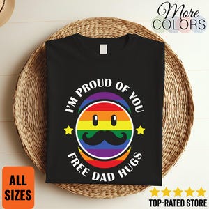 May include: Black t-shirt featuring a rainbow-coloured face graphic with a moustache, and the text "I'M PROUD OF YOU" and "FREE DAD HUGS". Two yellow stars are also present. The words "ALL SIZES" are in an orange box.