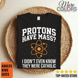 May include: A black t-shirt featuring white text that reads "PROTONS HAVE MASS? I DIDN'T EVEN KNOW THEY WERE CATHOLIC" and an orange graphic of an atom with orbiting electrons. The design is centered on the front of the shirt against a dark background.