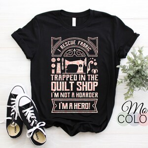 Peut inclure: T-shirt noir avec un motif rose et blanc qui dit "Je sauve le tissu piégé dans la boutique de courtepointes, je ne suis pas un thésauriseur, je suis un héros !" Le t-shirt est associé à des baskets noires et blanches. Les mots "Plus de couleurs" sont également visibles.