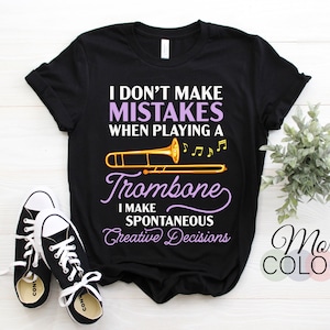 May include: Black t-shirt with a purple and white design that says "I don't make mistakes when playing a trombone. I make spontaneous creative decisions."