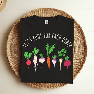 Peut inclure: T-shirt noir avec un graphique blanc de différents légumes et le texte "Let's Root For Each Other".