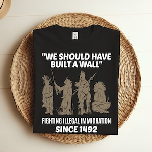 Op de afbeelding: Zwart T-shirt met een witte grafische print van Amerikaanse indianen en de tekst "We should have built a wall" en "Fighting illegal immigration since 1492".