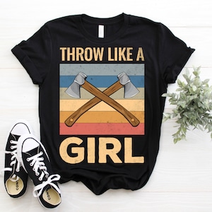 May include: Black t-shirt with a vintage-style graphic of two crossed axes and the text "THROW LIKE A GIRL".