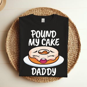 Puede incluir: Camiseta negra con texto blanco que dice "Pound My Cake Daddy" y una rosquilla de dibujos animados con cara.