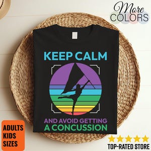 May include: Black t-shirt with the text "KEEP CALM AND AVOID GETTING A CONCUSSION" and a colorful graphic of a flag twirler. The design includes a rainbow-colored circle and is suitable for adults and kids.
