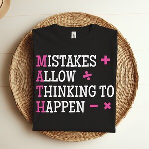 Pode incluir: Camiseta preta com texto branco que diz "MISTAKES + ALLOW ÷ THINKING TO HAPPEN - x". Os símbolos de adição, divisão, subtração e multiplicação estão em rosa.