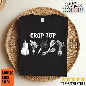 May include: Black crop top with the words "CROP TOP" in white. The shirt features a white illustration of various vegetables, including a squash, radish, carrot, leeks, and a turnip. The shirt is displayed on a woven basket.