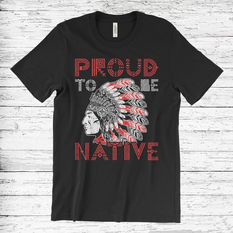 May include: Black t-shirt with the text "PROUD TO BE NATIVE" in red and white. The design features a Native American profile wearing a feathered headdress. The shirt is made of a soft material.