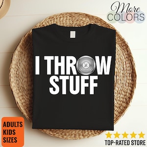 Puede incluir: Camiseta negra con el texto "I THROW STUFF" en letras blancas grandes. Un disco plateado sustituye la letra "O" de "THROW". La camiseta se muestra sobre una cesta tejida. Las palabras "ADULTS KIDS SIZES" están en un recuadro naranja.