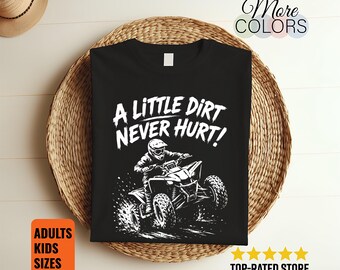 Può includere: Una t-shirt nera a maniche corte con una grafica bianca che raffigura una persona su un quad e il testo A LITTLE DIRT NEVER HURT! stampato sopra. Il disegno mostra il veicolo che solleva terra mentre il guidatore indossa un casco.
