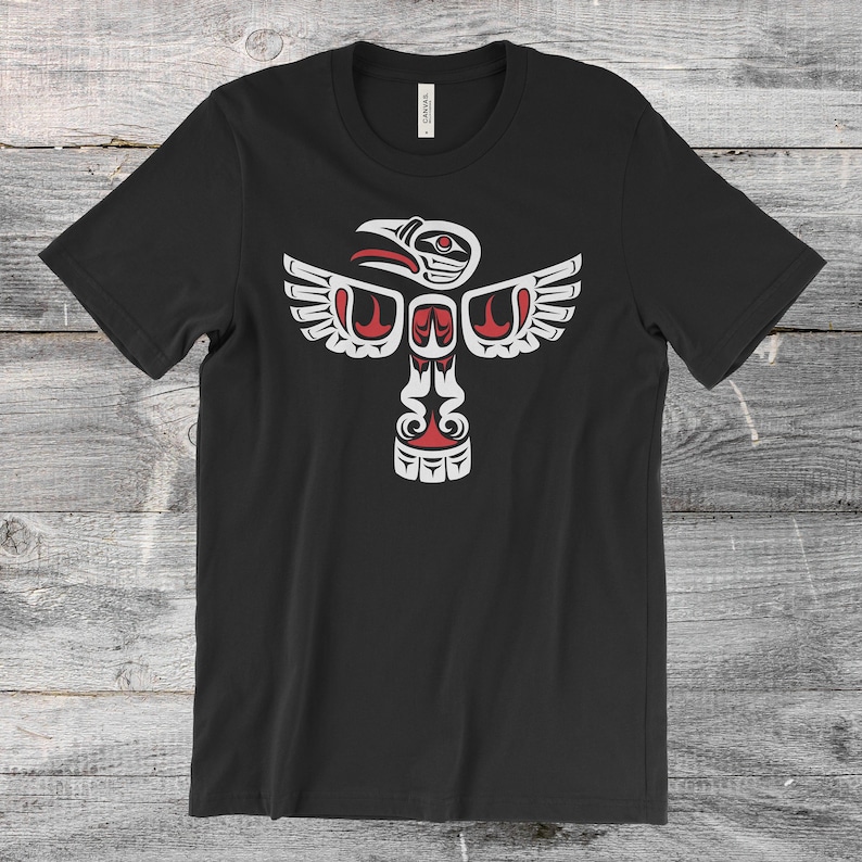 May include: Black t-shirt with a white and red stylized design of a bird with outstretched wings. The design is reminiscent of Native American art.