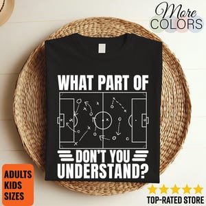 以下が含まれることがあります： 白いテキストとサッカーのプレー図が描かれた黒いTシャツ。「WHAT PART OF DON'T YOU UNDERSTAND？」と書かれています。Tシャツは編まれたバスケットの上に表示されています。追加のテキストは、大人と子供のサイズを示しています。
