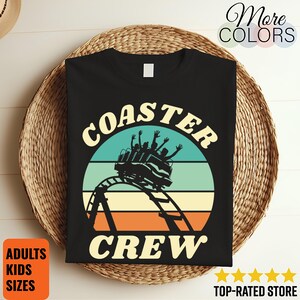 Peut inclure: T-shirt noir avec un motif rétro de montagnes russes et l'inscription "COASTER CREW". Le motif comprend un cercle turquoise, beige et orange. Le t-shirt affiche également les mots "ADULTS KIDS SIZES".