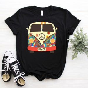 Puede incluir: Camiseta negra con un gráfico de furgoneta psicodélica colorida. La furgoneta tiene un signo de paz en la parte delantera y la palabra "Peace" escrita debajo.