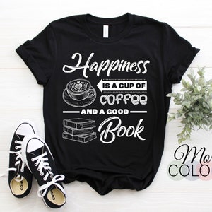 May include: Black t-shirt with the text "Happiness is a cup of coffee and a good book" in white script and block letters. The design includes a coffee cup with a heart-shaped design in the foam and a stack of books. Black and white sneakers are in the foreground.