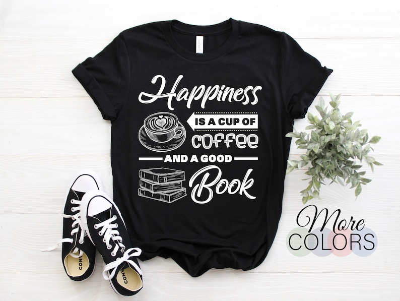 May include: Black t-shirt with the text "Happiness is a cup of coffee and a good book" in white script and block letters. The design includes a coffee cup with a heart-shaped design in the foam and a stack of books. Black and white sneakers are in the foreground.