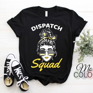 May include: Black t-shirt with the words "Dispatch Squad" in white and yellow. The graphic features a woman with sunglasses and a yellow headband. A pair of black and white sneakers are in the foreground.