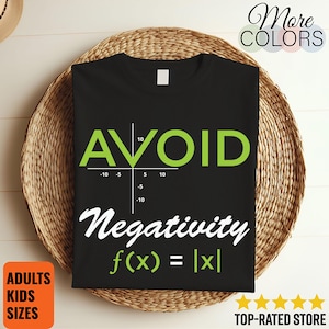 Puede incluir: Camiseta negra con la palabra "AVOID" en verde, un gráfico matemático y la frase "Negativity f(x) = |x|" en blanco. La camiseta se muestra sobre una cesta tejida. Las palabras "ADULTS KIDS SIZES" están en un cuadro naranja.