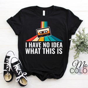 May include: Black t-shirt with a retro rainbow design and a cassette tape graphic. The text "I have no idea what this is" is printed on the shirt.