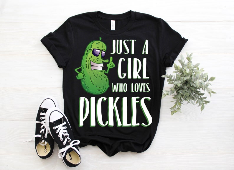 Może przedstawiać: Czarny t-shirt z zielonym kresk&oacute;wkowym og&oacute;rkiem w okularach przeciwsłonecznych i tekstem "Just a girl who loves pickles".