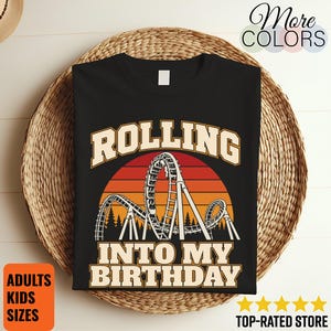Könnte beinhalten: Ein schwarzes T-Shirt mit einer Grafik einer Achterbahn vor einem Sonnenuntergang. Der Text lautet ROLLING INTO MY BIRTHDAY in einer fetten, hellen Schrift. Das Design enthält Silhouetten von Bäumen an der Basis der Achterbahnstruktur.